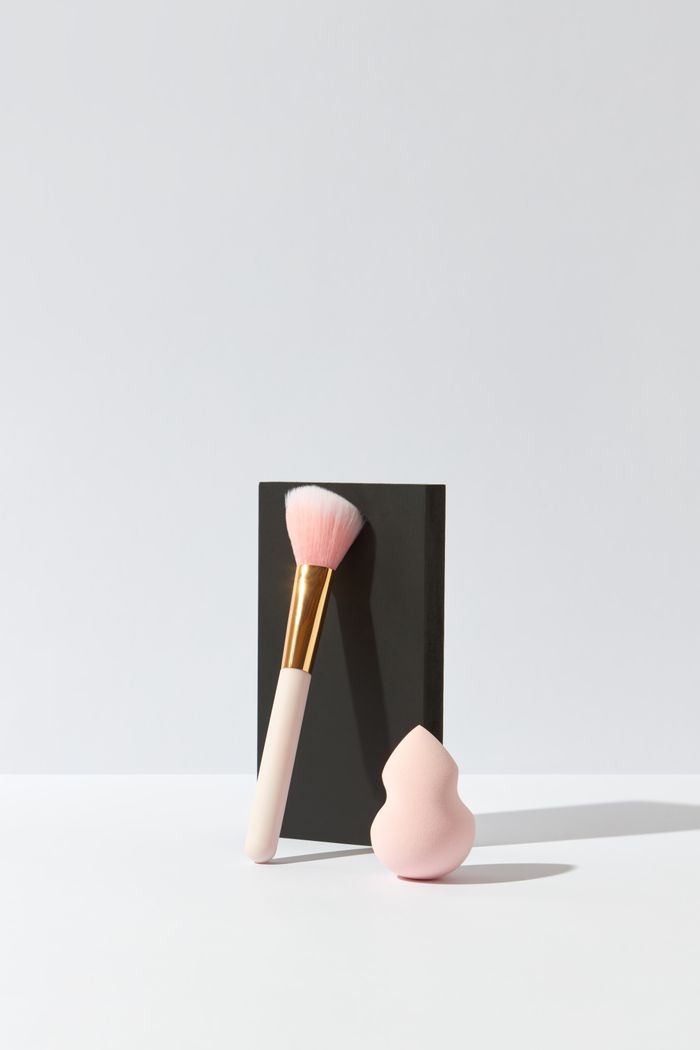 who-we-are Elegant minimalist composition of a makeup brush and sponge blender on a white surface with a black background.