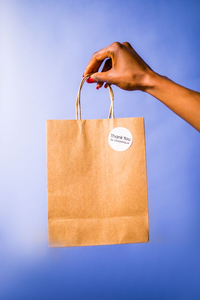 services-hero A hand holds a thank you paper bag against a vibrant blue background.