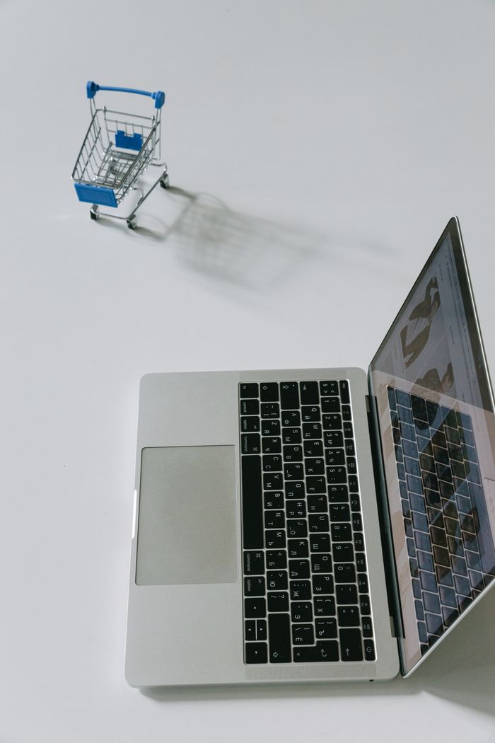 services-04 Minimalist scene of a laptop beside a miniature shopping cart symbolizing online shopping.